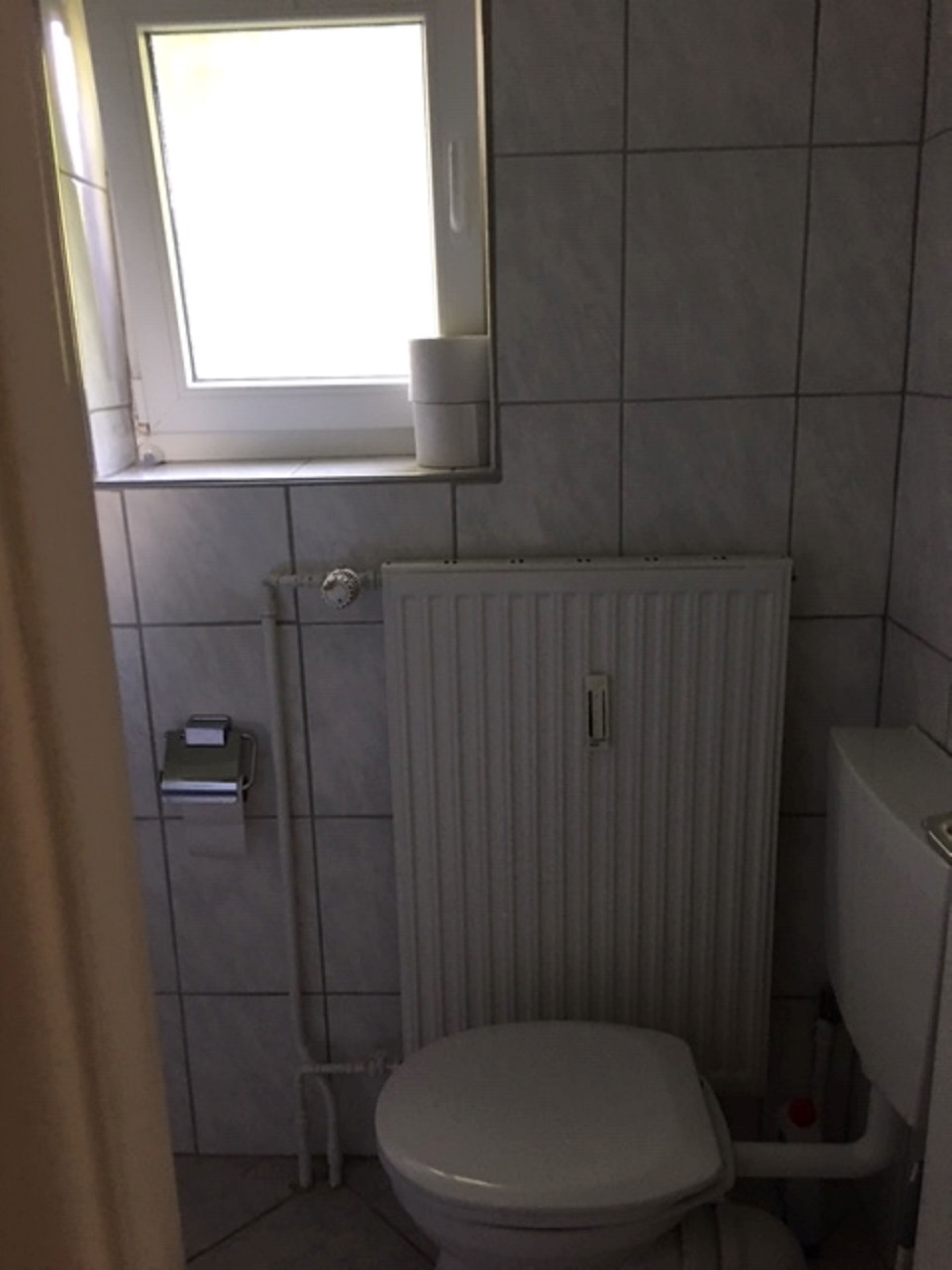 Un baño pequeño con un inodoro, un radiador y una ventana.