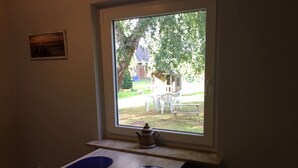Une pièce avec une fenêtre donnant sur un jardin, une petite table avec une théière et un radiateur.