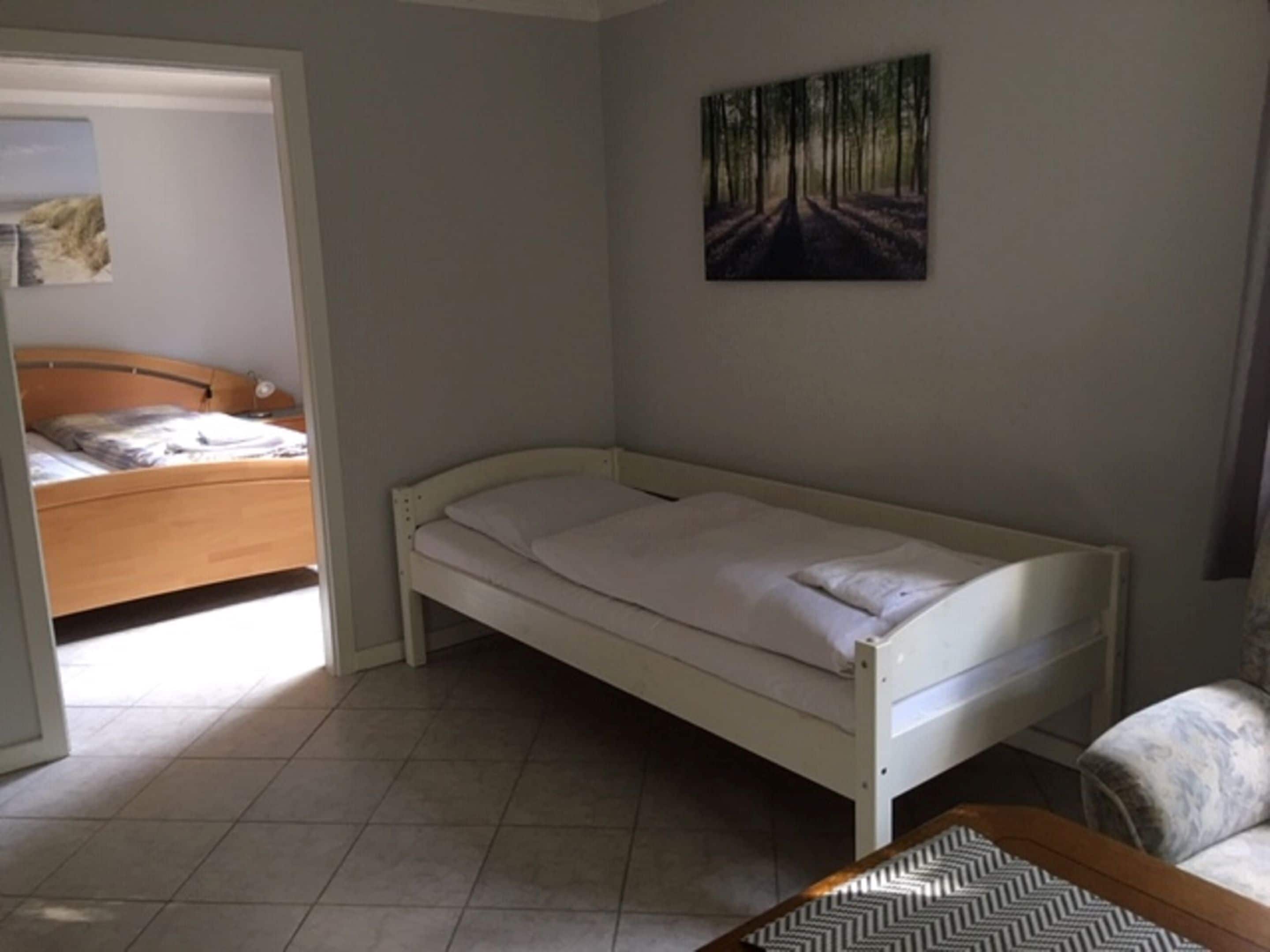 Una habitación pequeña con cama individual, cabecera de madera, colchón blanco y una mesa con estampado de espiga.