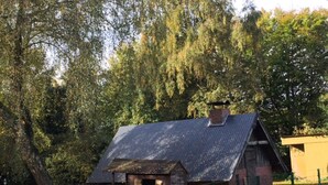Une cabane en bois rustique, surmontée d’un toit en métal, entourée d’une clôture verte et d’arbres.