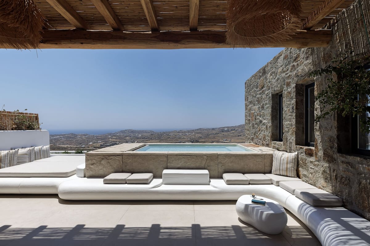 Une terrasse sur le toit avec une piscine, des sièges blancs rembourrés et un bâtiment en pierre doté de fenêtres.