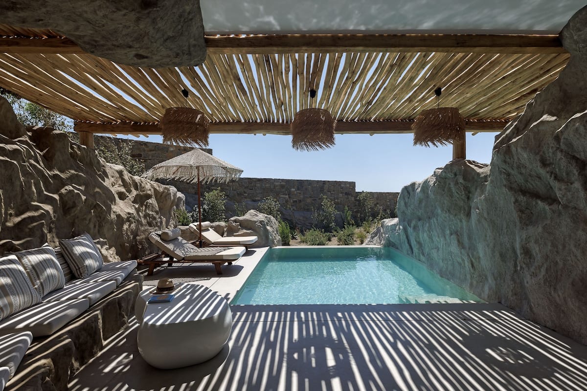 Un espace piscine privatif, doté de chaises longues et d’un banc en pierre, entouré de murs rocheux et d’une pergola en bois.