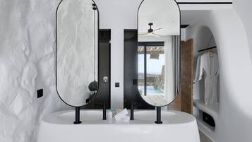 A modern bathroom with two large mirrors, a white sink, and a view of a cliff through a glass door.