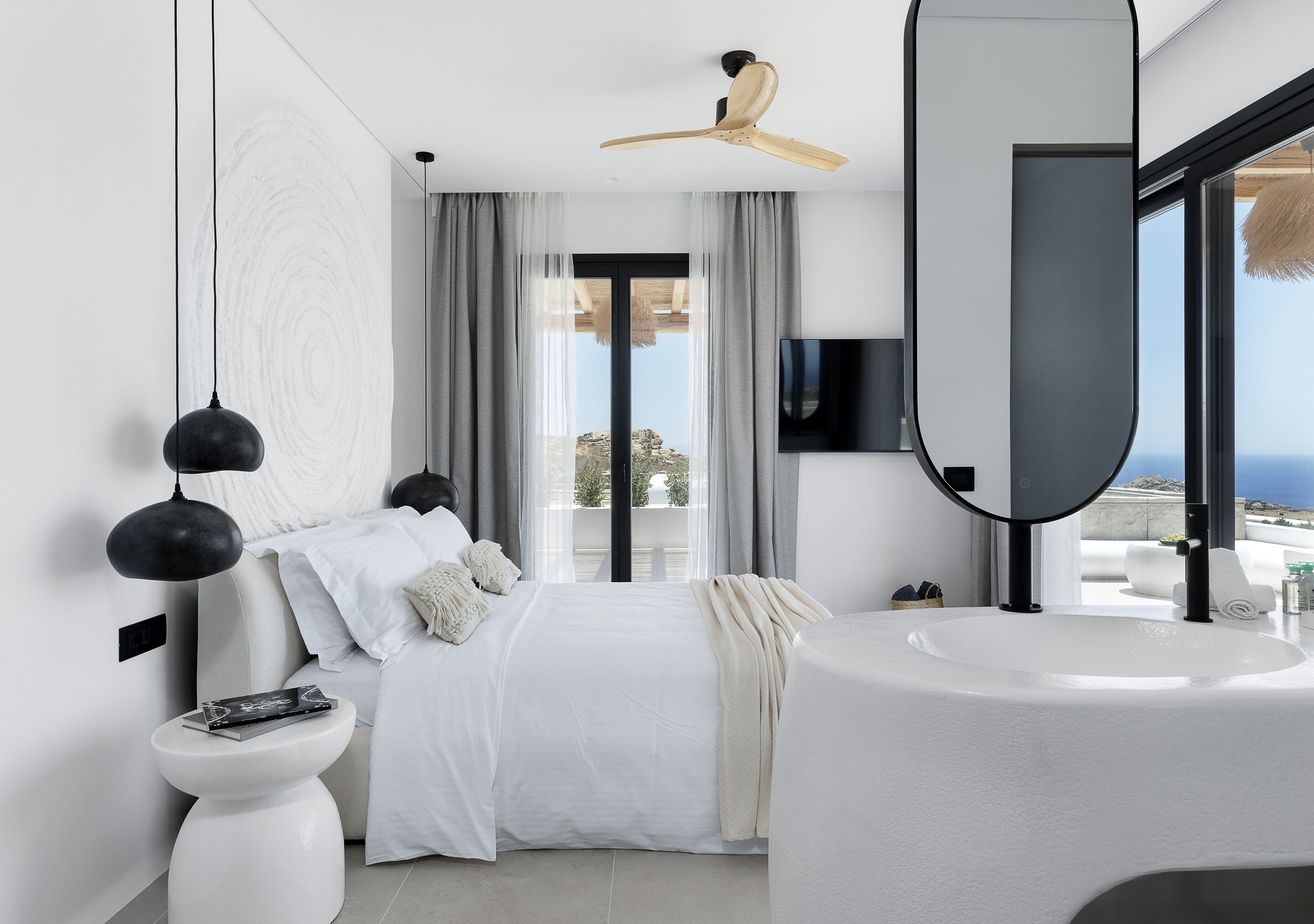 A modern bedroom with a bed, a white sink, a ceiling fan, and a large window with a view.