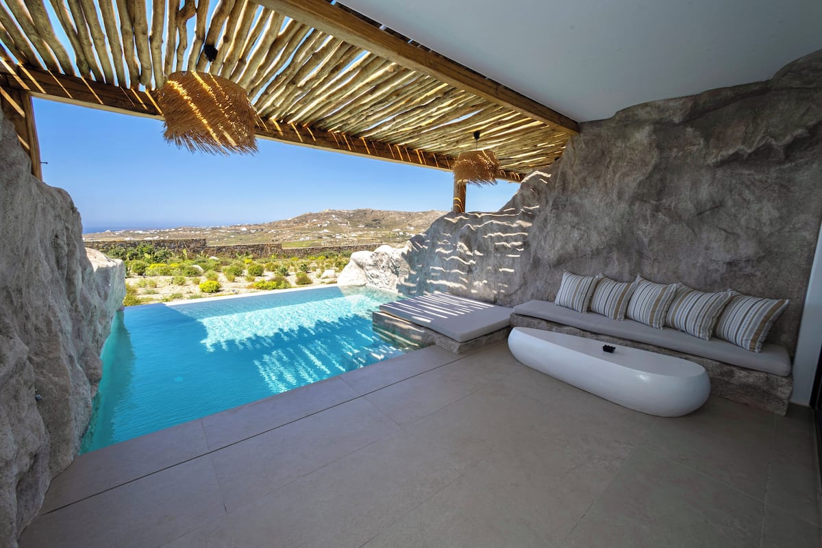 Un espace piscine extérieur moderne, agrémenté d’un mur en pierre, d’une pergola en bois et d’un banc blanc avec des coussins à rayures.