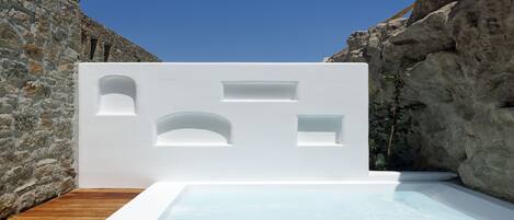 A modern outdoor hot tub with a white exterior, set against a stone wall and a rocky cliff.