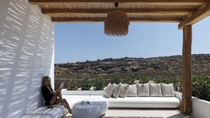 A modern outdoor seating area with a white sofa and cushions, a unique white chair, and a hanging light fixture. - WhiteArt Suites (Mykonos)