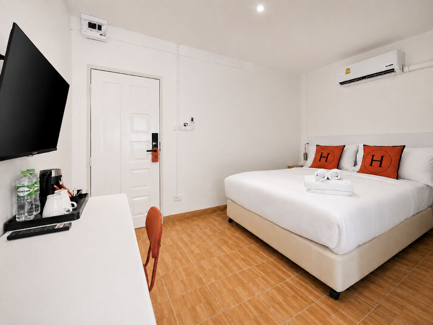 A hotel room with a bed, a desk with a coffee maker, a TV, and an air conditioner.