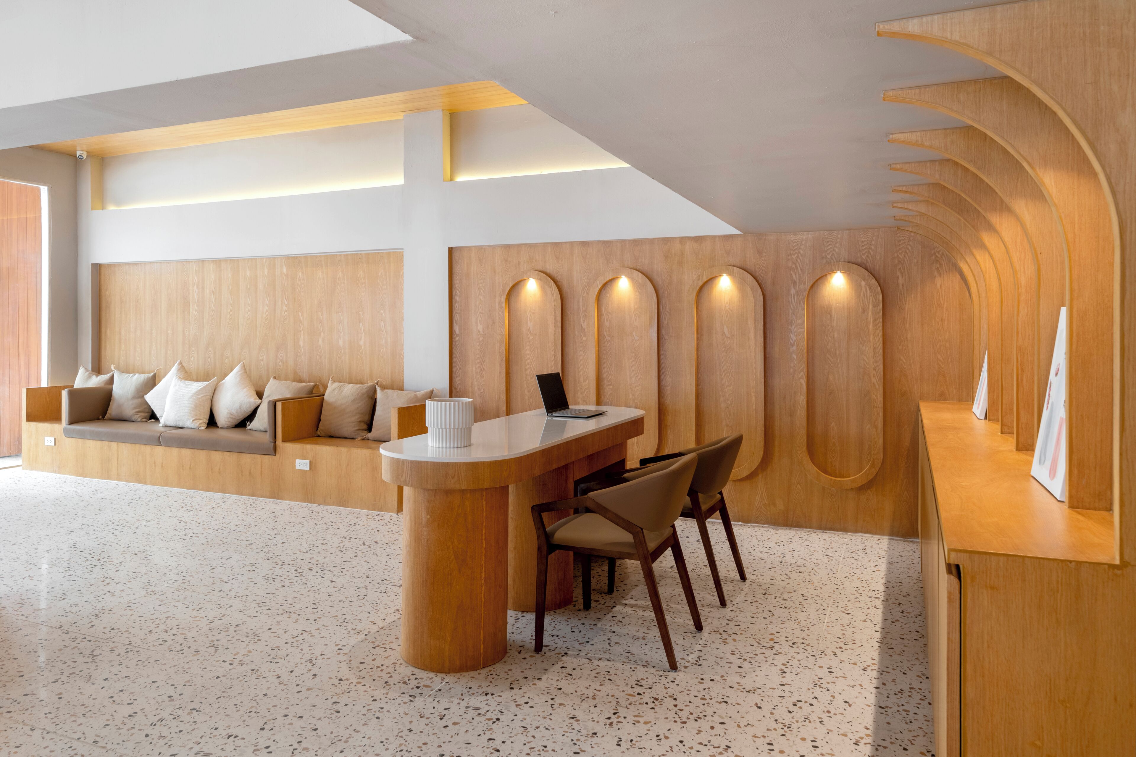 A modern reception area with a wooden reception desk, seating area, and a wall with built-in niches.