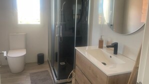 Un baño moderno con cabina de ducha de vidrio, inodoro blanco, tocador de madera con lavabo blanco y un espejo grande.