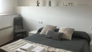 Un dormitorio con una cama, una silla, un ventilador de techo y una estantería con objetos decorativos.