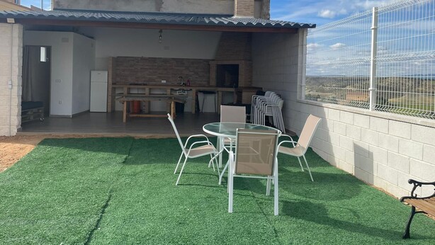 Un patio al aire libre con chimenea de ladrillo, una mesa de comedor con sillas y un área cercada.