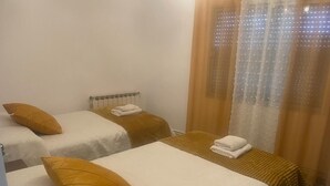 Una habitación con dos camas, cada una con una colcha blanca y una almohada amarilla.