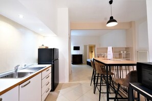 A modern kitchen with a central island, a dining area with bar stools, and a visible refrigerator.