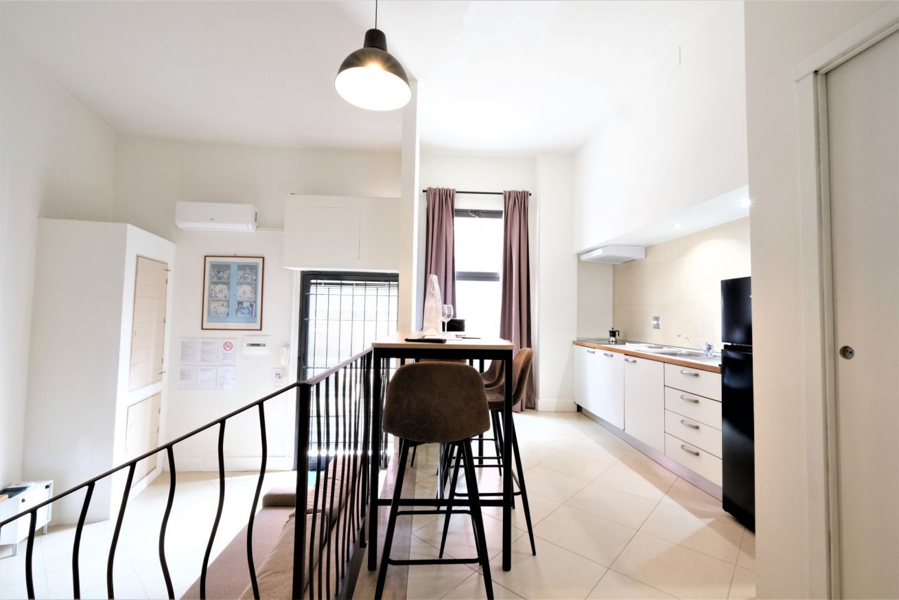 A modern kitchen with a dining area, featuring a kitchen island, a refrigerator, and a hanging light fixture.