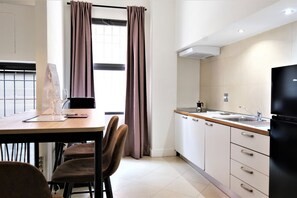 A modern kitchen with white cabinets, a black refrigerator, and a window with curtains.