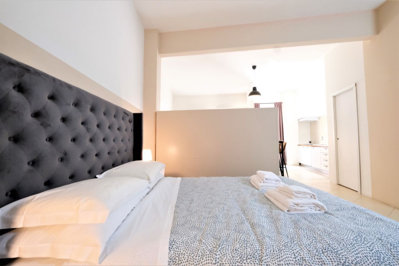 A modern bedroom with a tufted headboard, a neatly made bed with white linens, and a patterned bedspread.