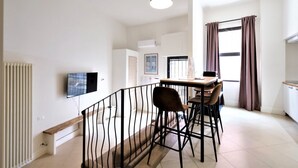 A modern apartment with a dining area, a TV mounted on the wall, and a kitchen visible in the background. - Wine Apartments Florence Amarone (Firenze)