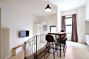 A modern apartment with a dining area, a TV mounted on the wall, and a kitchen visible in the background. - Wine Apartments Florence Amarone (Firenze)