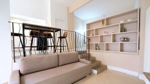 A living room with a beige sofa, a staircase with a black railing, and a bookshelf with various items. - Wine Apartments Florence Amarone (Firenze)