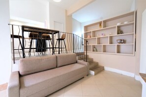 A living room with a beige sofa, a staircase with a black railing, and a bookshelf with various items. - Wine Apartments Florence Amarone (Firenze)