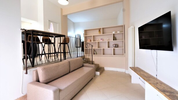 A modern living room with a sofa, a TV mounted on the wall, and a staircase with chairs. - Wine Apartments Florence Amarone (Firenze)