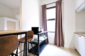A small, clean room with a desk, chairs, a computer, and a window with curtains.