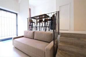 A modern living room with a beige sofa, a dining table with chairs, and a staircase.