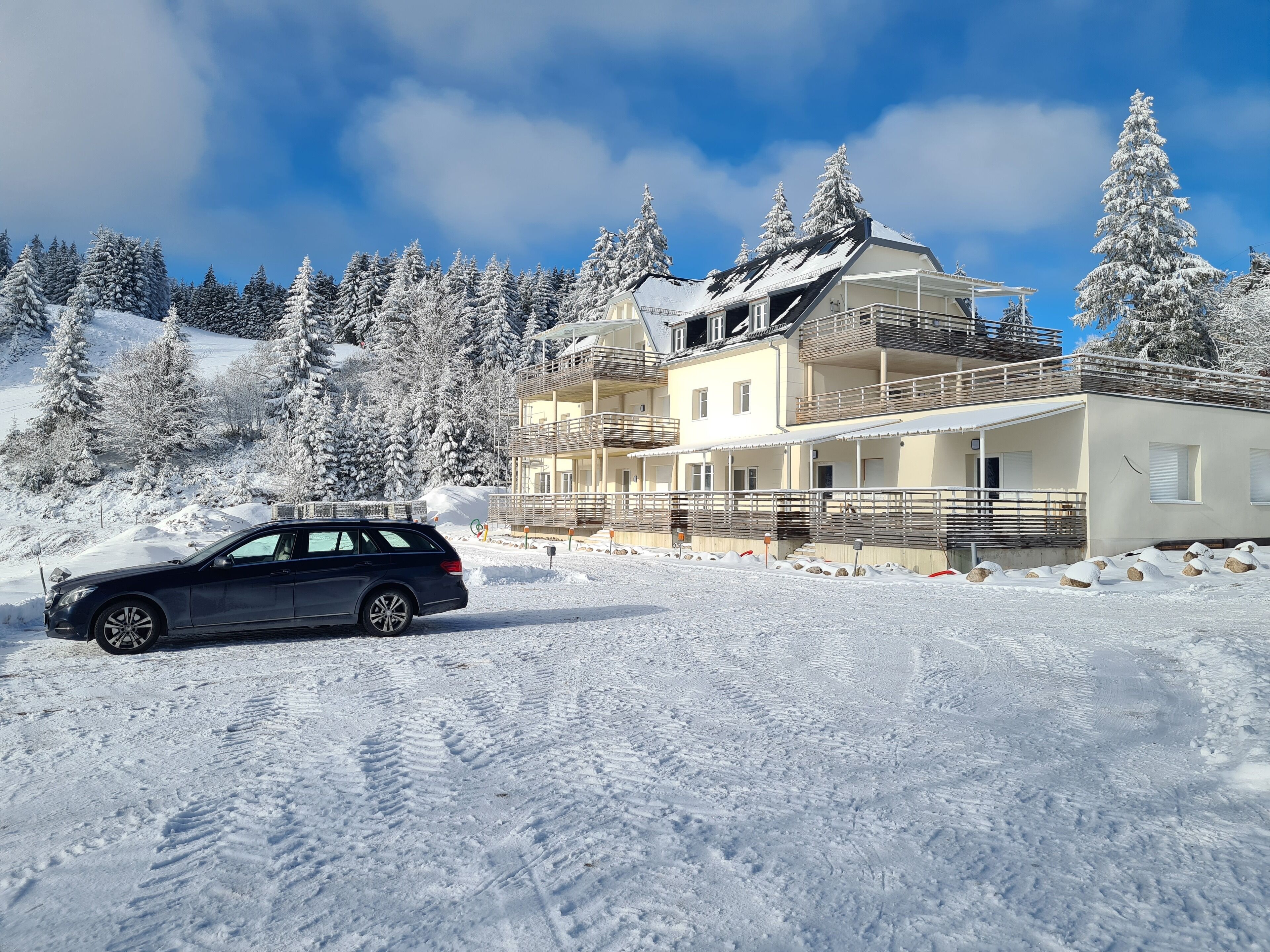 Ein mehrstöckiges Gebäude mit Balkonen, umgeben von schneebedeckten Bäumen und einem klaren Himmel.