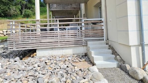 Un bâtiment doté d’un porche en béton, d’une clôture en bois et d’un escalier menant à une porte.