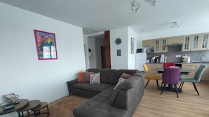 Un salon avec un canapé gris, une table à manger avec des chaises et un coin cuisine doté de meubles en bois et d’un four à micro-ondes.