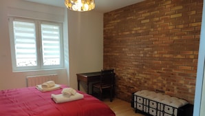 Une chambre avec un mur en briques, un lit avec une literie rouge, un bureau et une commode.