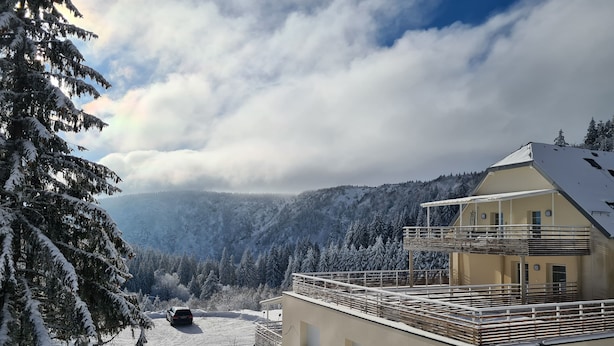 Un paysage montagneux enneigé avec un bâtiment doté d’un balcon et une voiture garée à proximité.