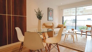 A modern living room with a glass coffee table, white and beige chairs, a sofa, and a potted plant. - w* | Sophisticated 2BR with Balcony in Miraflores (Lima)