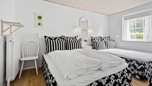 Ein Schlafzimmer mit Bett, Nachttischen, einem Sessel, einem Heizkörper, einem Fenster und einem Spiegel.