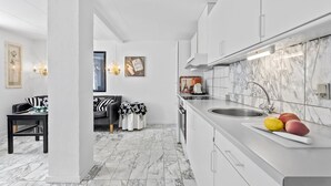 Eine moderne Küche mit weißen Schränken, einer Marmor-Spritzschutzwand und einem Essbereich mit einem schwarz-weißen Sofa.