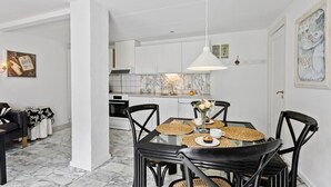 Eine moderne Küche mit weißen Schränken, einer Marmor-Spritzschutzwand und einem Essbereich mit einem Glastisch und schwarzen Stühlen.