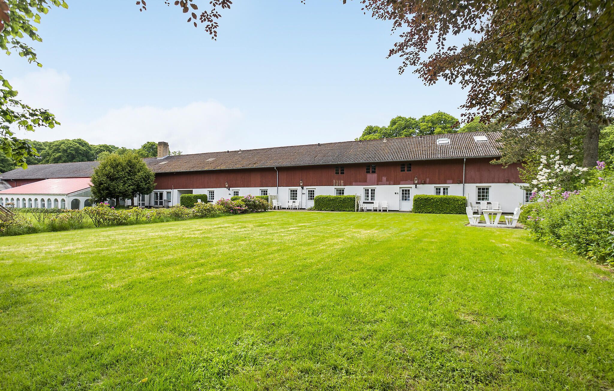 A large, single-story building with a red roof and white walls, surrounded by a well-maintained lawn and trees.
