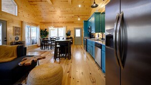 L’intérieur d’une cabane est doté de planchers en bois, d’un coin repas, d’une cuisine avec des meubles bleus et d’un grand réfrigérateur.