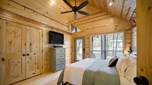 Une chambre dans une cabane en bois, équipée d’un lit, d’une télévision et d’un ventilateur de plafond.
