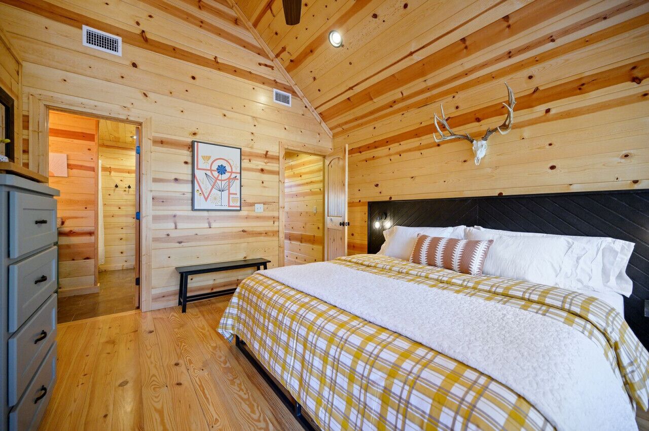 A wooden cabin bedroom with a bed, a bench, and a deer head mounted on the wall.