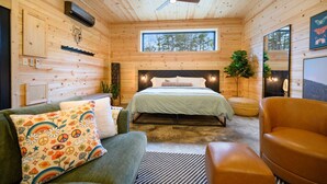 Een knus houten slaapkamer met een groot bed, een plafondventilator, een raam en uitzicht op het bos.