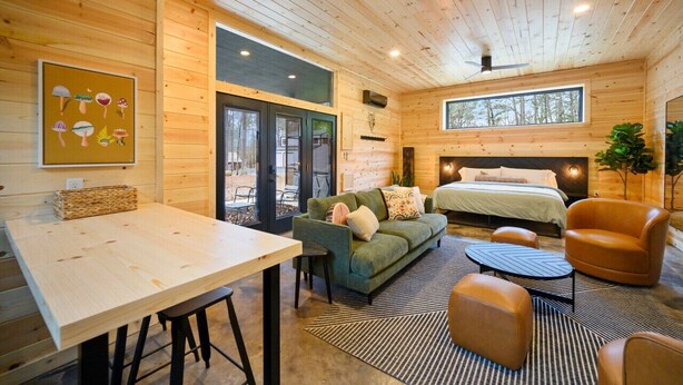 Een gezellig chaletinterieur met houten details, een eethoek, een bank, een bed en een groot raam.