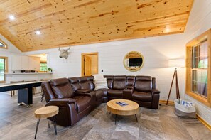 A spacious living area with a leather sectional sofa, a round wooden coffee table, and a stone-tiled floor.