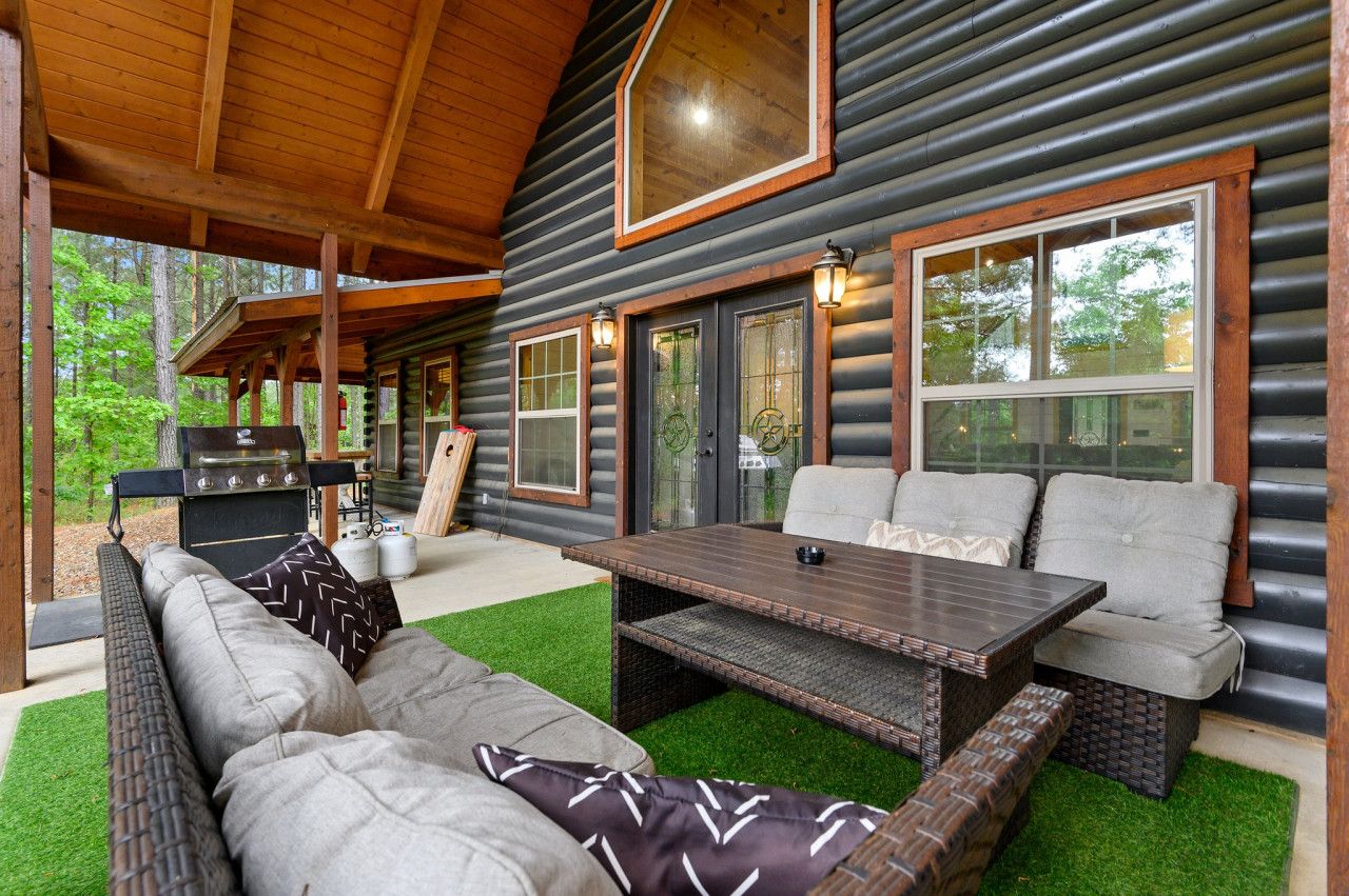 A log cabin with a covered patio, outdoor seating, and a grill.