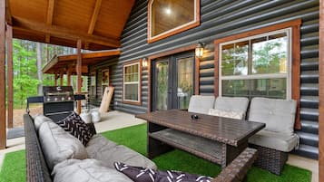 A log cabin with a covered patio, outdoor seating, and a grill.