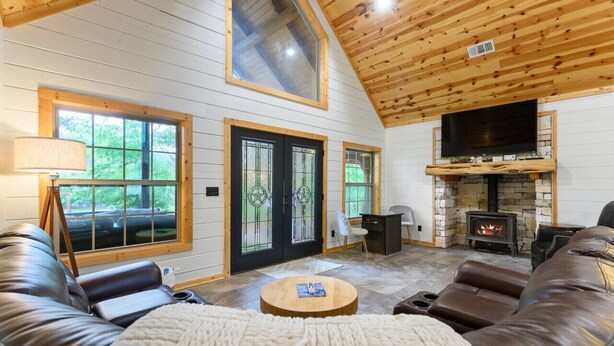 Ein gemütliches Blockhäuschen-Interieur mit Kamin aus Stein, Ledersofas und großen Fenstern.
