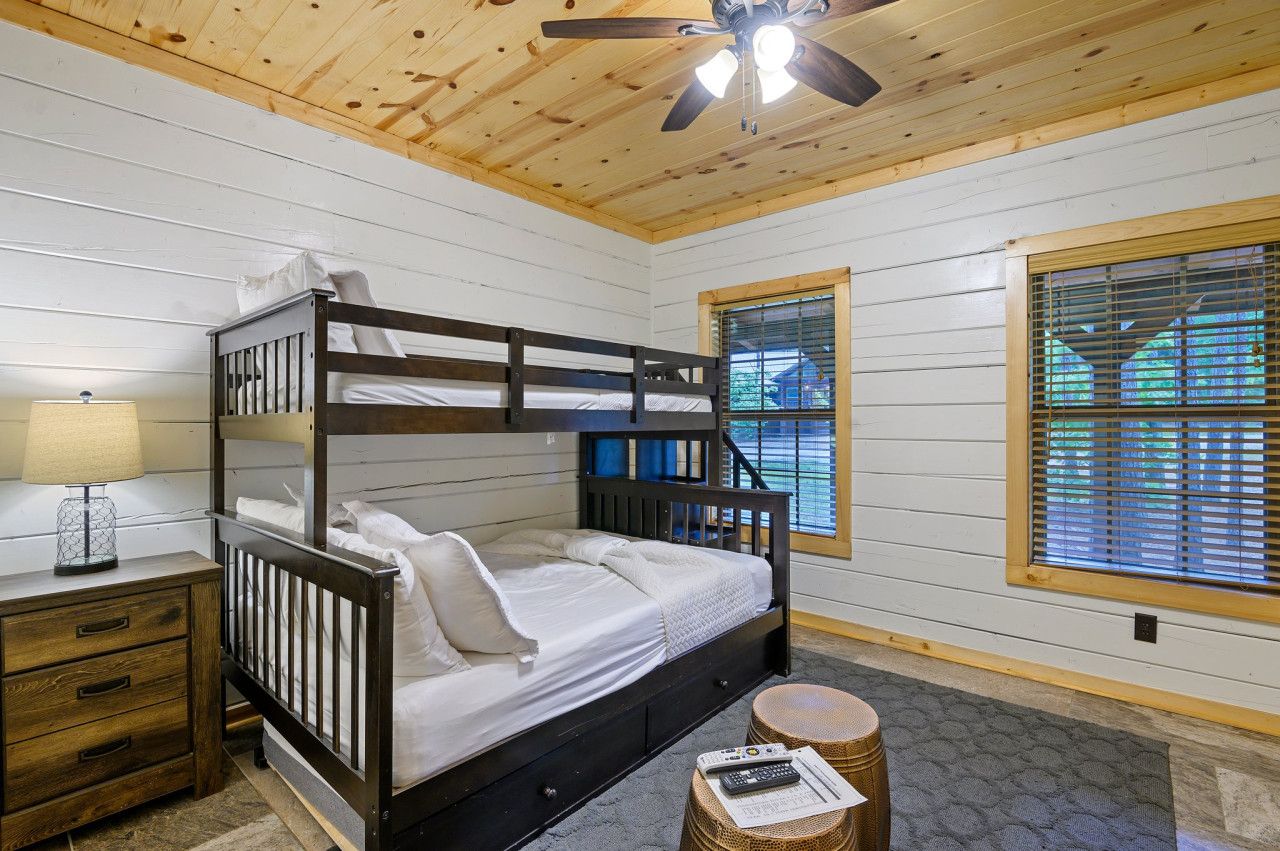 A bunk bed with a wooden headboard, a bedside table with a lamp, and a window with blinds.