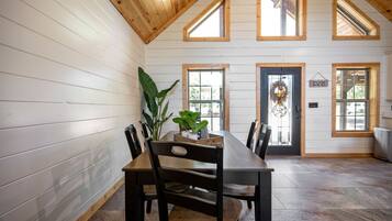 A dining area with a wooden table and chairs, a potted plant, and a door with a wreath.