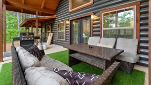 Eine Blockhütte mit einer überdachten Terrasse, Sitzgelegenheiten im Freien und einem Grill.
